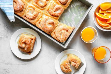 烤盘里的橙子早餐卷，放在小盘子里，旁边是几杯橙汁和一碗橙子片